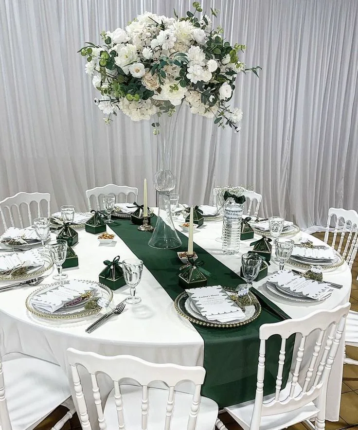 A white and green wedding table styled with a tall floral centrepiece and gold details